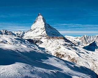 Schneebedeckte Gebirgslandschaft mit markantem spitzen Gipfel unter blauem Himmel.