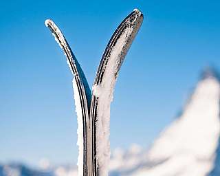 Gros plan sur deux skis avec de la neige devant un ciel bleu.